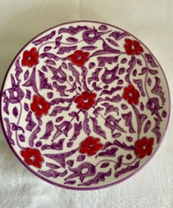 Assiette en céramique artisanale avec motifs floraux rouges et violets, fabriquée à la main par des artisans marocains