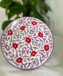 Assiette en céramique artisanale avec motifs floraux rouges et violets, fabriquée à la main.
